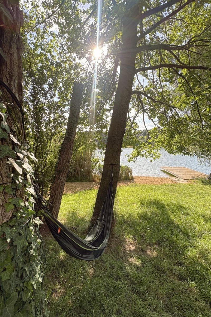 Hojdacia sieť medzi stromami s výhľadom na jazero a mólo v podvečernom slnku
