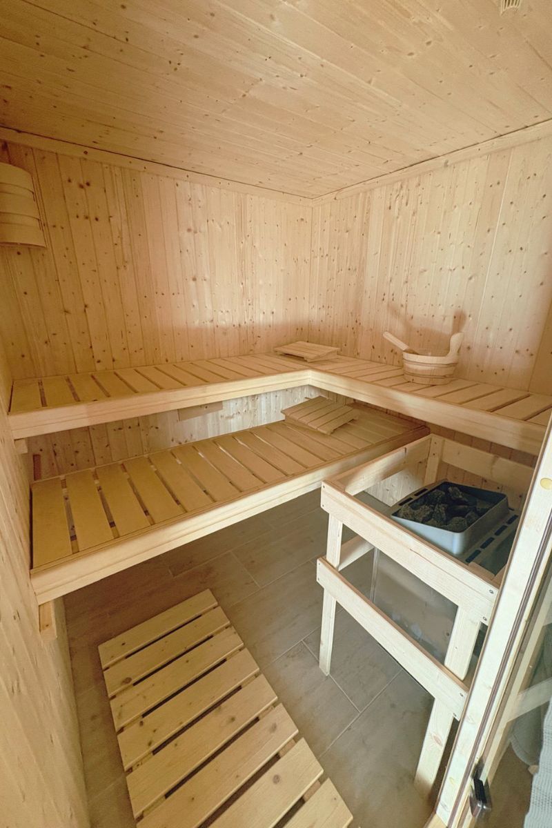 Fínska sauna z borovicového dreva — vnútro s rohovými lavicami a kachľami